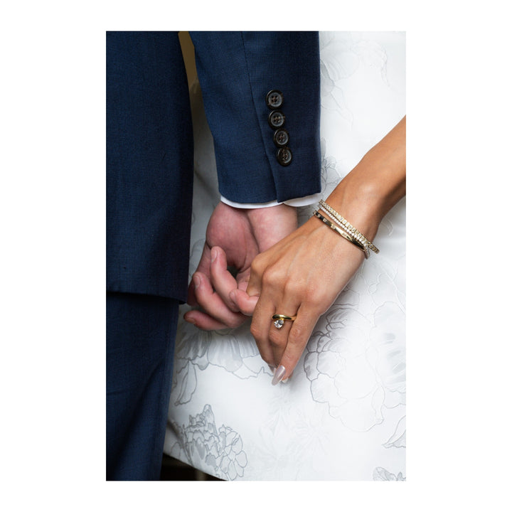 Couple holding hands, bride wearing a Caroline Signature 14K yellow gold engagement ring with a diamond.