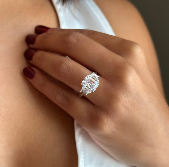 Charlotte three-stone engagement ring with a 2 CT emerald-cut diamond, trapezoid side stones, and a two-tone setting.
