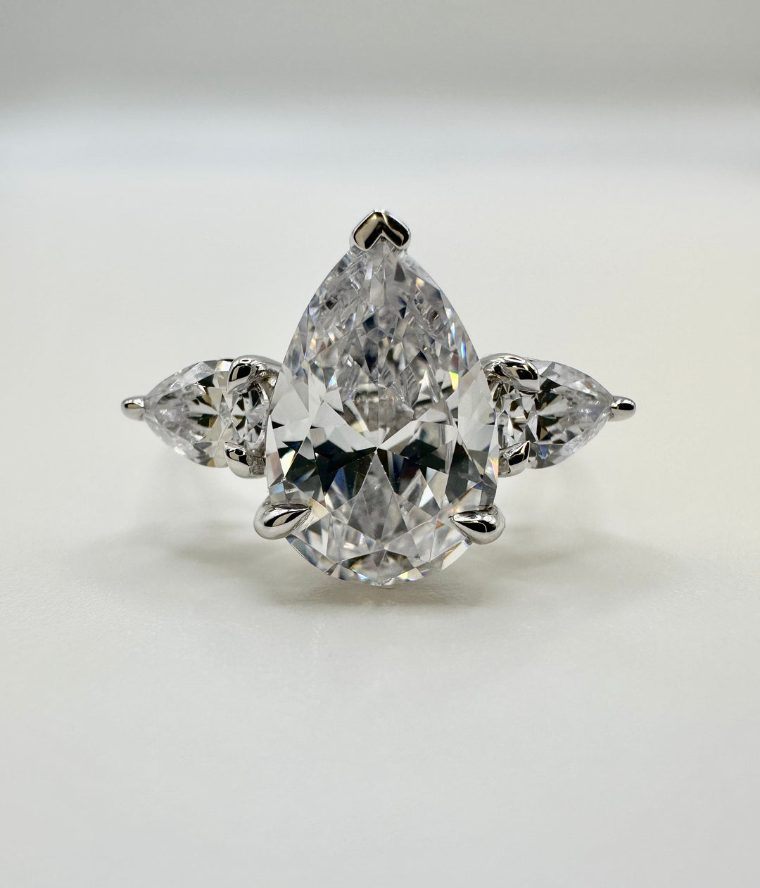 Silver engagement ring with a large pear-shaped center diamond flanked by two smaller pear diamonds.
