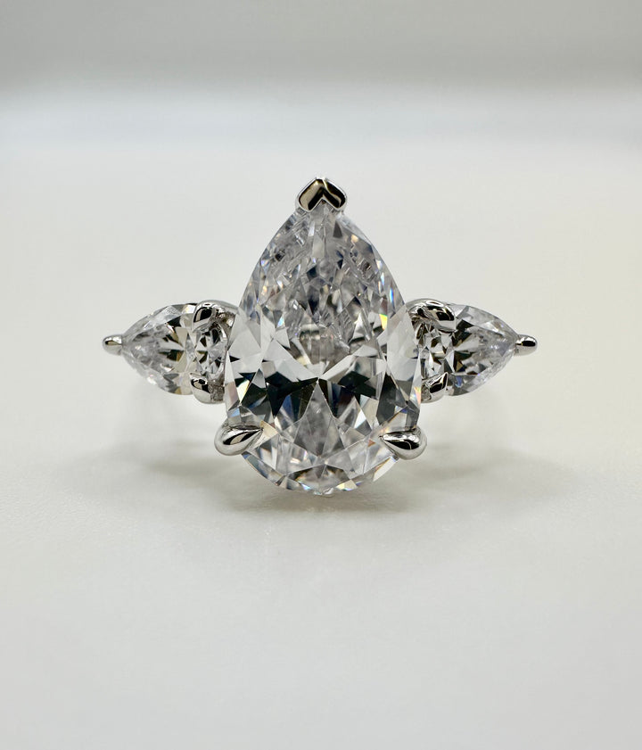 Silver engagement ring with a large pear-shaped center diamond flanked by two smaller pear diamonds.