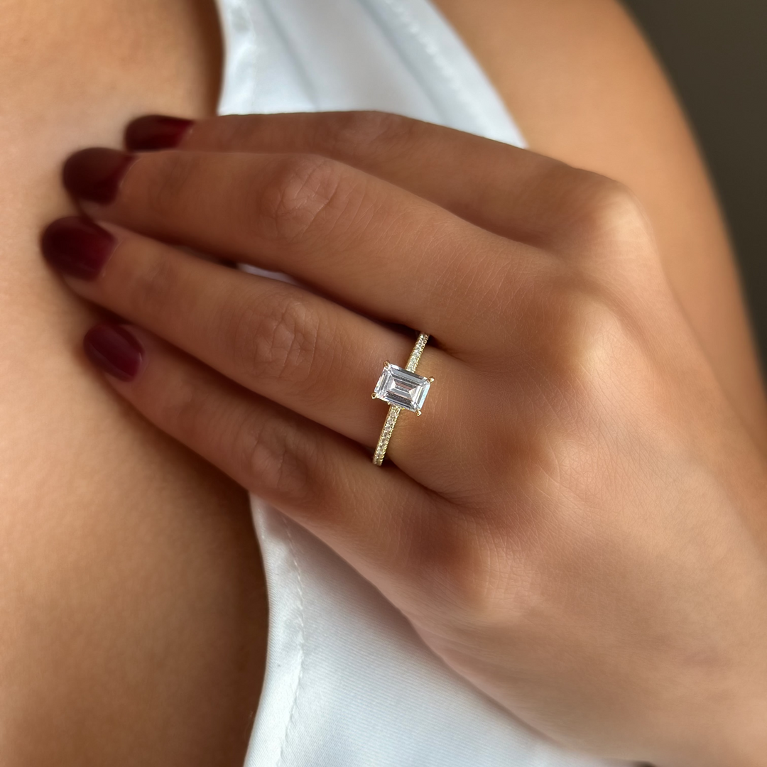 Poppy solitaire engagement ring with an emerald-cut diamond center and pavé yellow gold band.